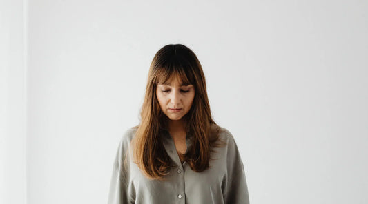 Woman with long hair looking down thoughtfully against a plain white background, symbolizing introspection and vitality representing the connection between mitochondrial health and energy.