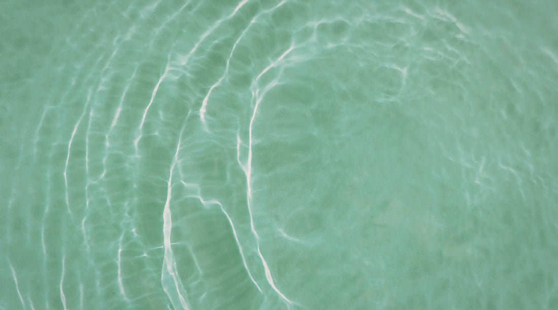 Soft ripples of clear green water reflecting sunlight, symbolising hydration, calm, and gentle summer wellbeing inspired by nature.