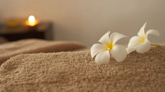 Frangipani flowers on a towel in a serene spa setting with a glowing candle, symbolising stress relief, daily wellness, and the calming benefits of adaptogens like Ashwagandha