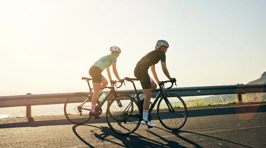 Two cyclists riding on a scenic mountain road at sunrise, representing an active lifestyle and seasonal wellness in September.