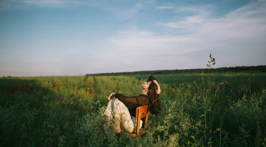 Woman relaxing on a wooden chair in a field of wildflowers under a blue sky, symbolising balance, mindfulness, and slow living.
