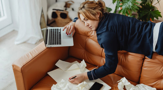 Woman feeling mentally overwhelmed while working from home, surrounded by digital devices and notes, representing information overload, mental fatigue, digital overwhelm, stress, and the impact of constant stimulation on wellbeing.