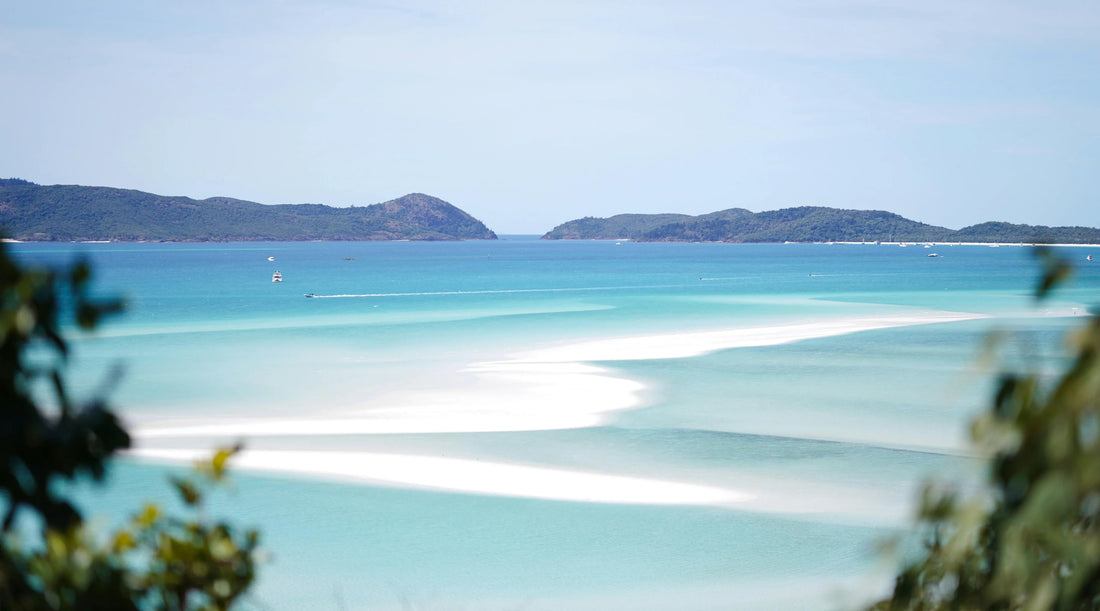 A serene coastal landscape with turquoise ocean waters, white sandbanks, and distant green islands under a clear blue sky, evoking calm, balance, and a slow summer rhythm inspired by nature.
