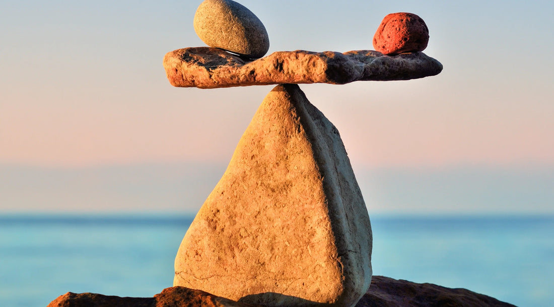 Balanced stones carefully stacked against a calm ocean horizon, symbolising summer balance, regulation, and steady wellbeing over motivation, reflecting a gentle, sustainable approach to seasonal wellness.