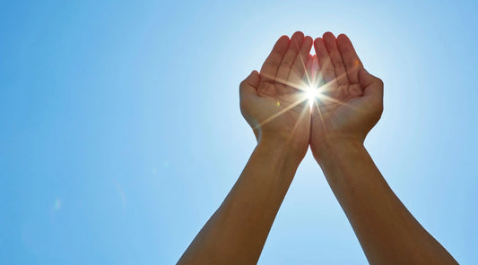 Hands gently cupping sunlight against a clear blue sky, symbolising summer vitality, hydration, rest, and the foundational systems that support balance, energy, and wellbeing during warmer months.