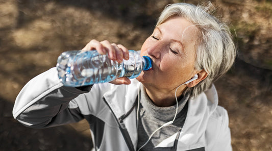 Older woman drinking water outdoors after exercise, illustrating everyday hydration and electrolyte needs during physical activity.