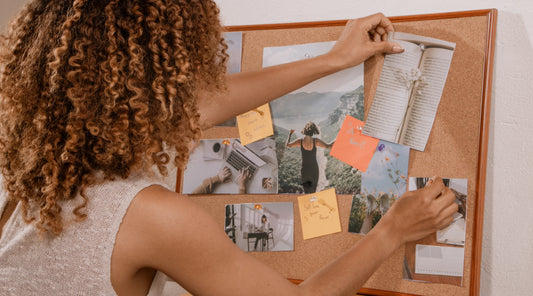 Woman creating a vision board with photos, notes and wellbeing reminders, representing mindful planning, intentional living, healthy routines and setting realistic wellness goals for everyday balance.