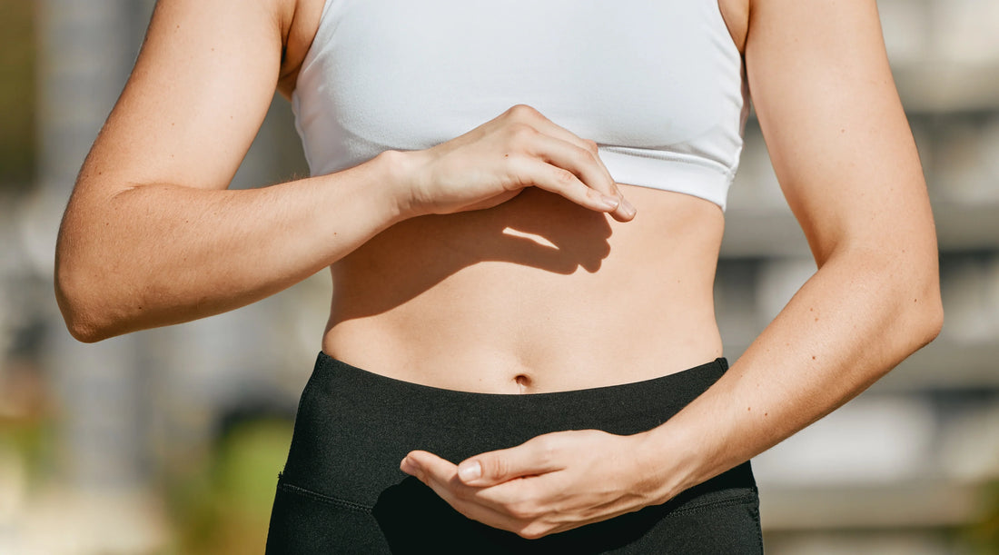 Woman in activewear holding her hands around her stomach, representing dietary fibre, gut health and healthy digestion.