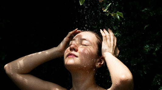 Person standing beneath a gentle outdoor shower with water flowing over their face, symbolising an end-of-winter wellness reset, stress relief, mindful self-care, and preparing the body and mind for a healthy transition into spring.