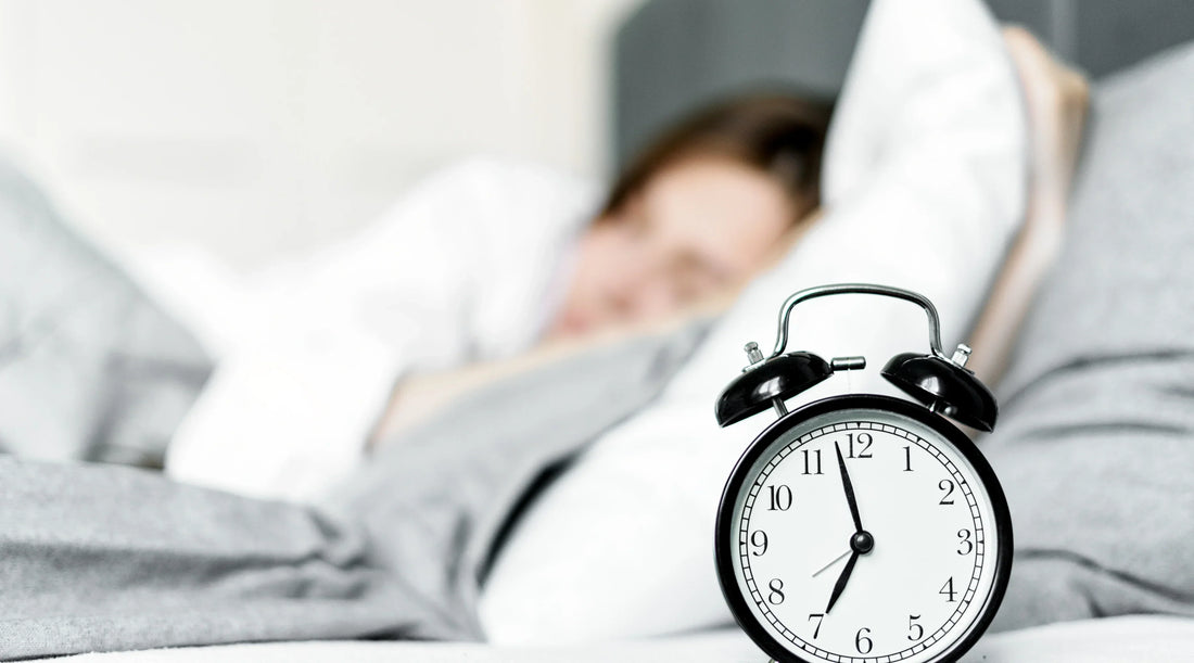 Woman sleeping beside an alarm clock, representing healthy sleep habits, better rest and a calming bedtime routine for overall wellbeing.