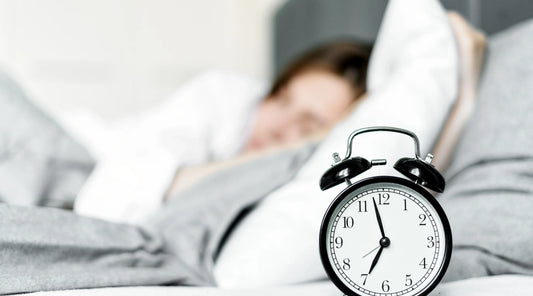 Woman sleeping beside an alarm clock, representing healthy sleep habits, better rest and a calming bedtime routine for overall wellbeing.